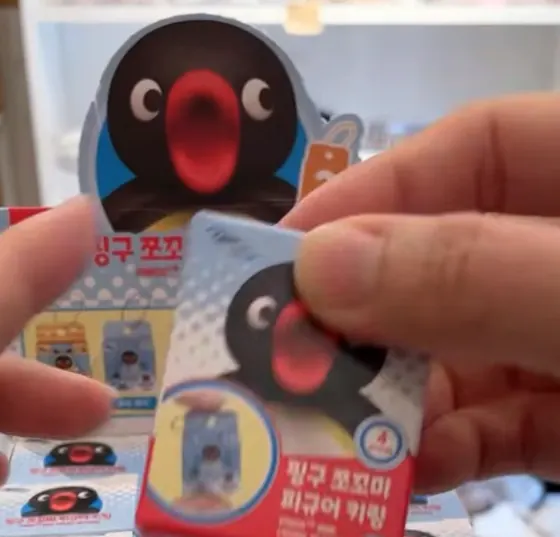 손에 든 핑구 쪼꼬미 피규어 키링 상자와 뒤에 쌓인 같은 상자들
